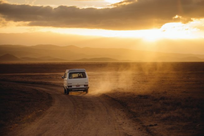 Car driving on dusty road into the sunset